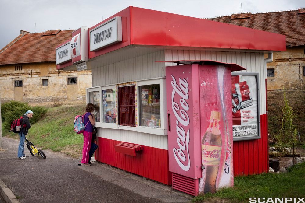 To barn i Tsjekkia står utanfor ein gammal kiosk med ein gammal Coca Cola-automat på utsida. Foto. 