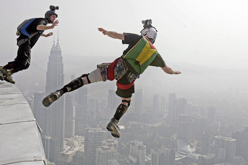 Foto av to personer som har fallskjerm på ryggen og hopper fra taket på en skyskraper