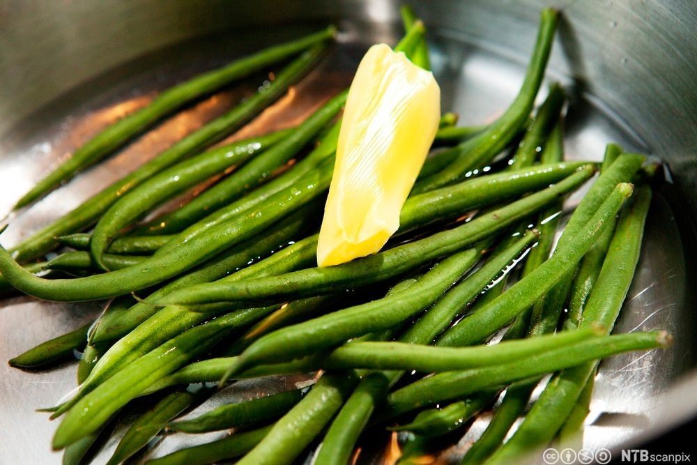Aspargesbønner i en kasserolle med en smørklatt. Foto.