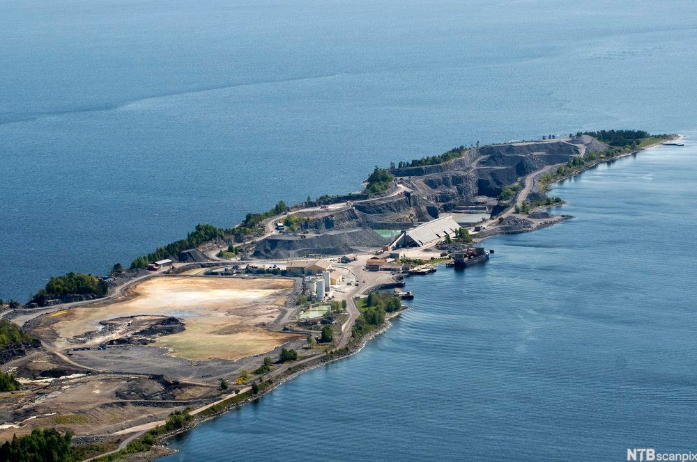 Foto av lang og smal øy med veier, grustak, tankanlegg og kai.