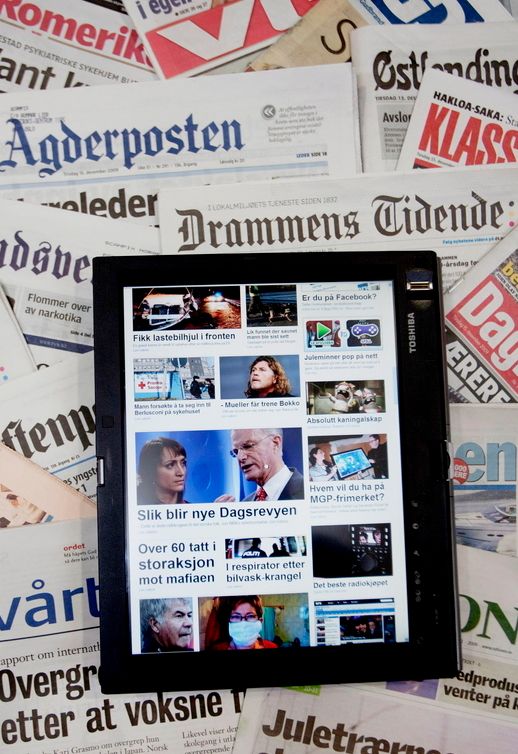 Eit nettbrett viser framsida til ei nettavis. Nettbrettet ligg oppå mange papiraviser. Foto.