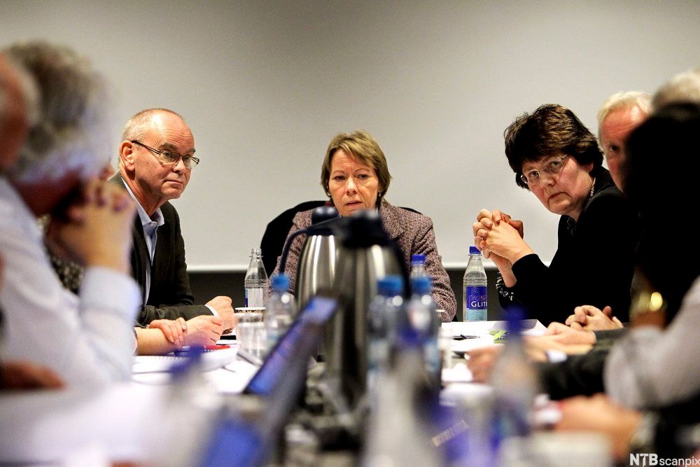 Alvorlige ansikter rundt et møtebord. Foto. 