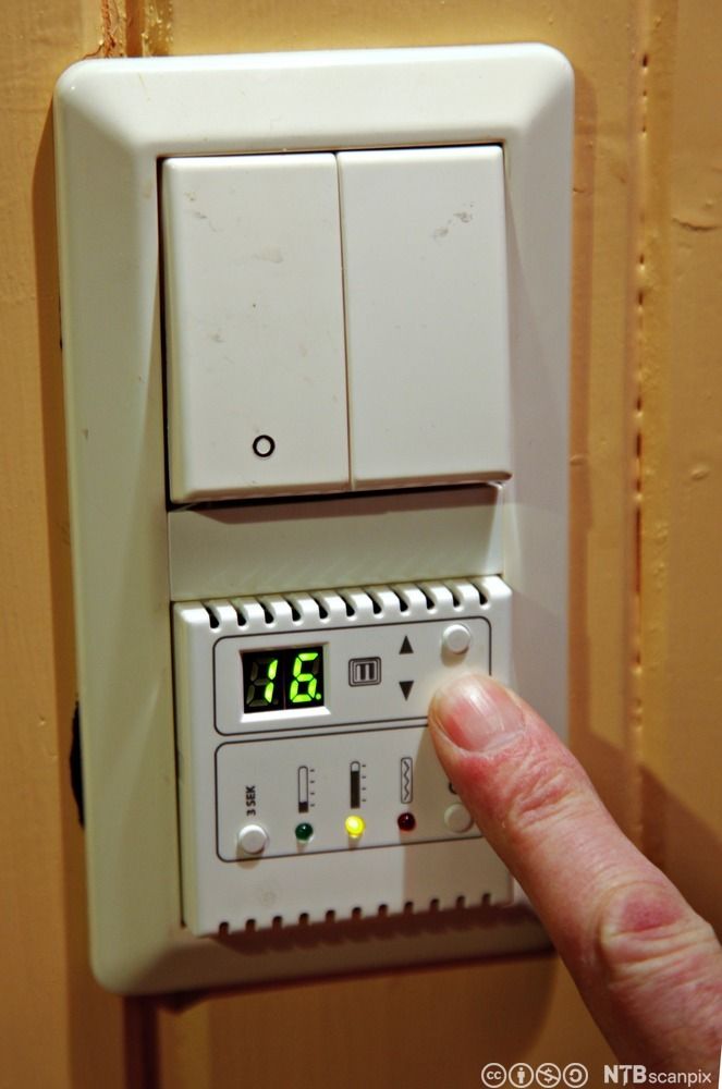 Nærbilde av en finger som stiller inn en termostat. Foto.