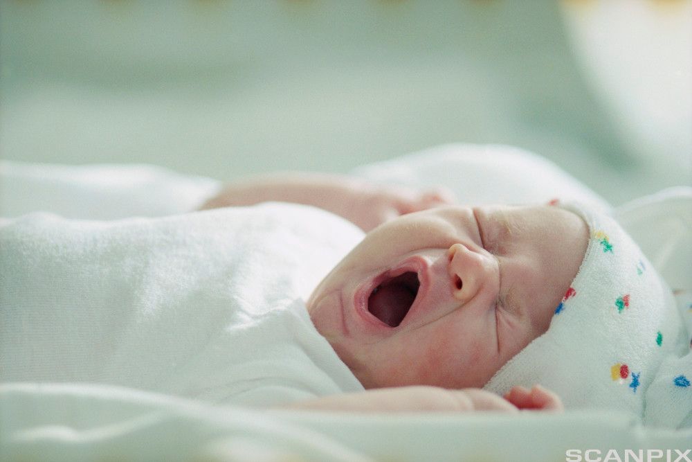 Baby som ligger i en seng og gjesper. Foto.