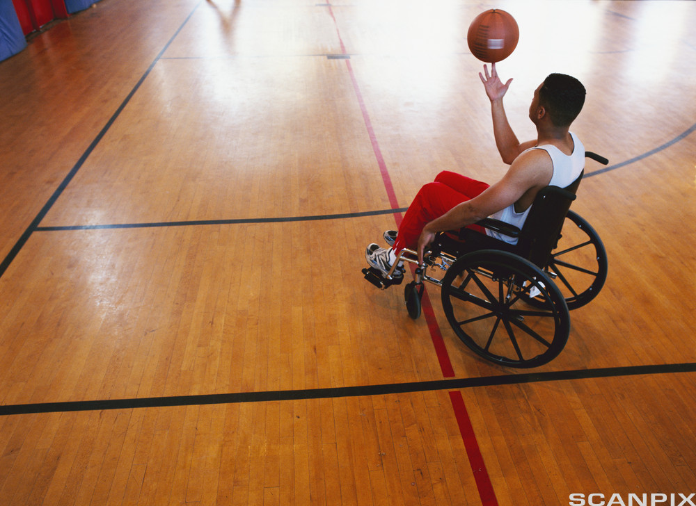 Mann i rullestol i gymsal med basketball. Foto.