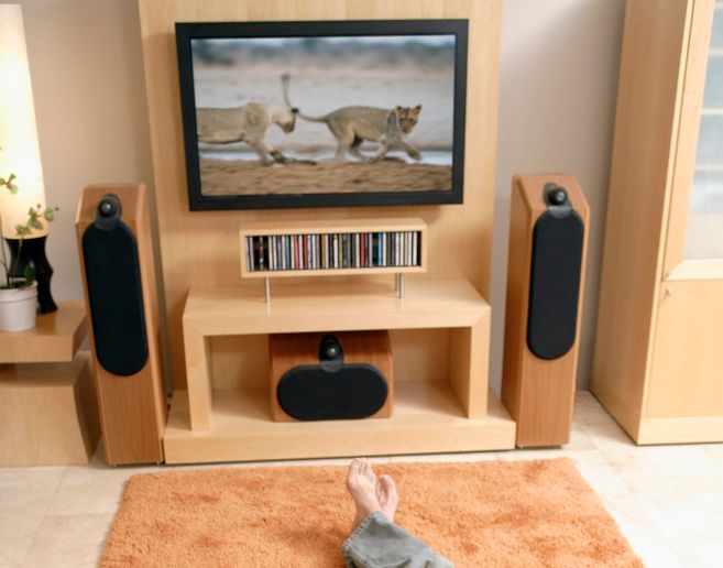 To bein på eit teppe framfor ein tv med høgtalarar under og på sidene. Foto.