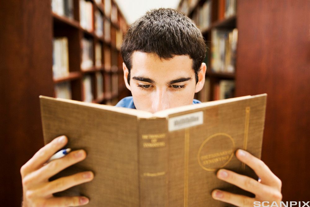Mann leser i ei bok på biblioteket. Foto.