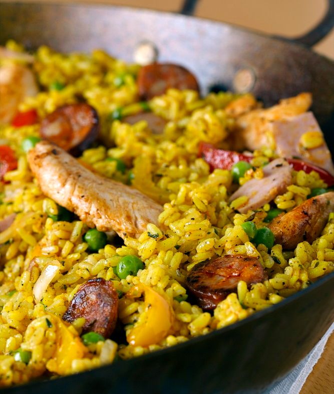 Paella i ei panne. Retten er fargerik med gul ris, grønne erter, rød paprika og biter av stekt kjøtt. Foto.