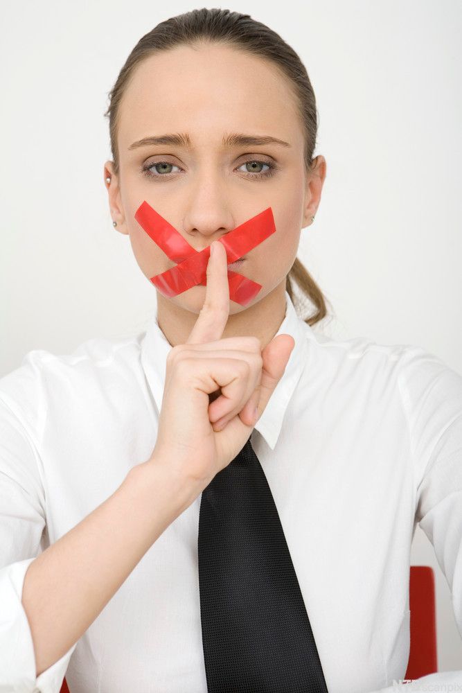Kvinne med rød tape over munnen som hysjer med fingeren. Foto.
