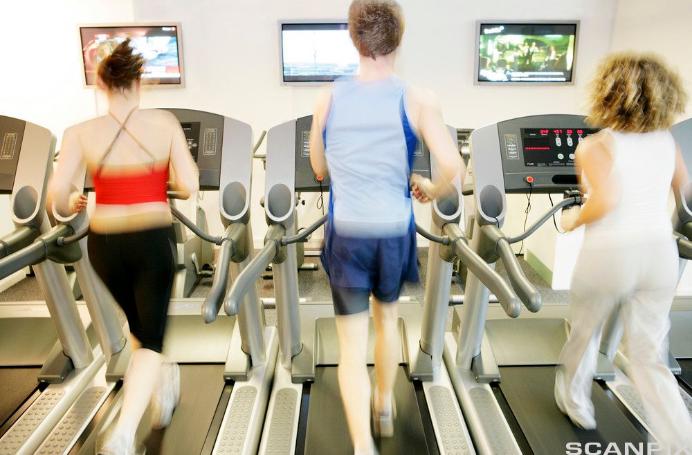 Ein mann og to kvinner løper på tredemøller. På veggen framfor dei er det skjermar. Foto.