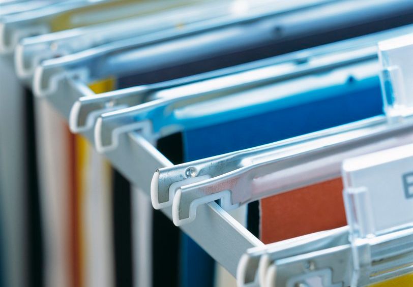 Fysiske arkivmapper i ulike farger på rekke og rad i et arkivskap. Foto.