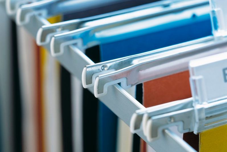 Fysiske arkivmapper i ulike fargar på rekke og rad i eit arkivskap. Foto.