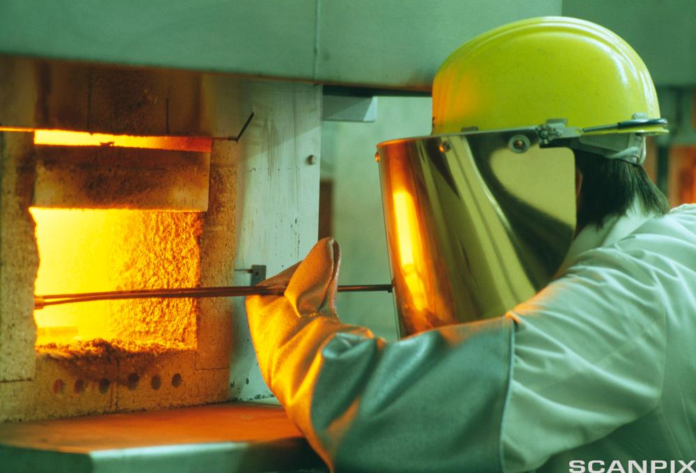Arbeider ved smelteovn med skikkerhetsutstyr. Foto.