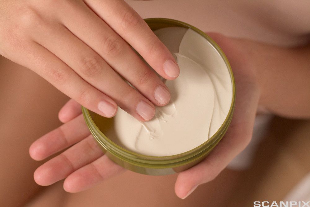 En hånd holder en boks med krem. Foto.