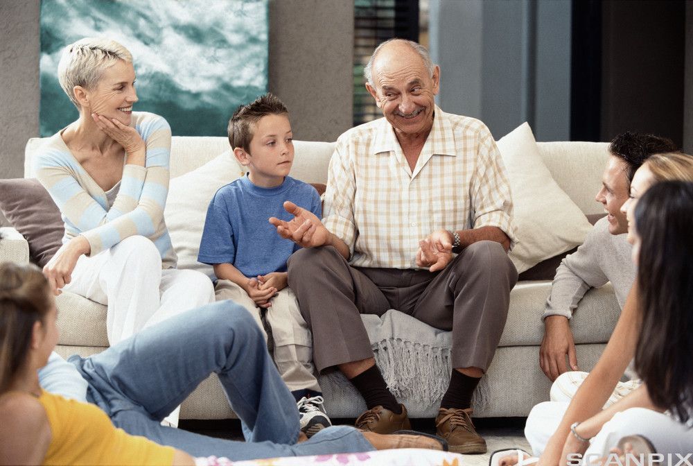Bestefar forteller noe til familien som sitter rundt ham. Foto.