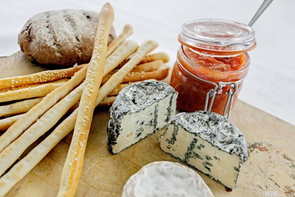 Blåmuggost, rabarbra- og gulrotmarmelade, grissini og brød på ei trefjøl. Foto.