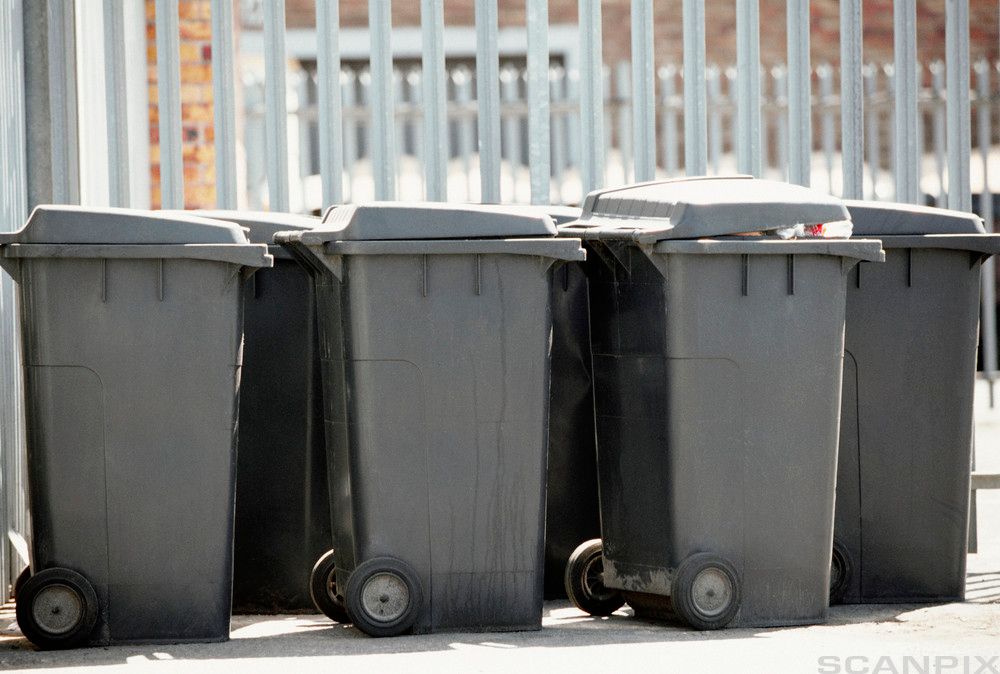 Søppeldunker på rekke utenfor et gjerde. Foto.