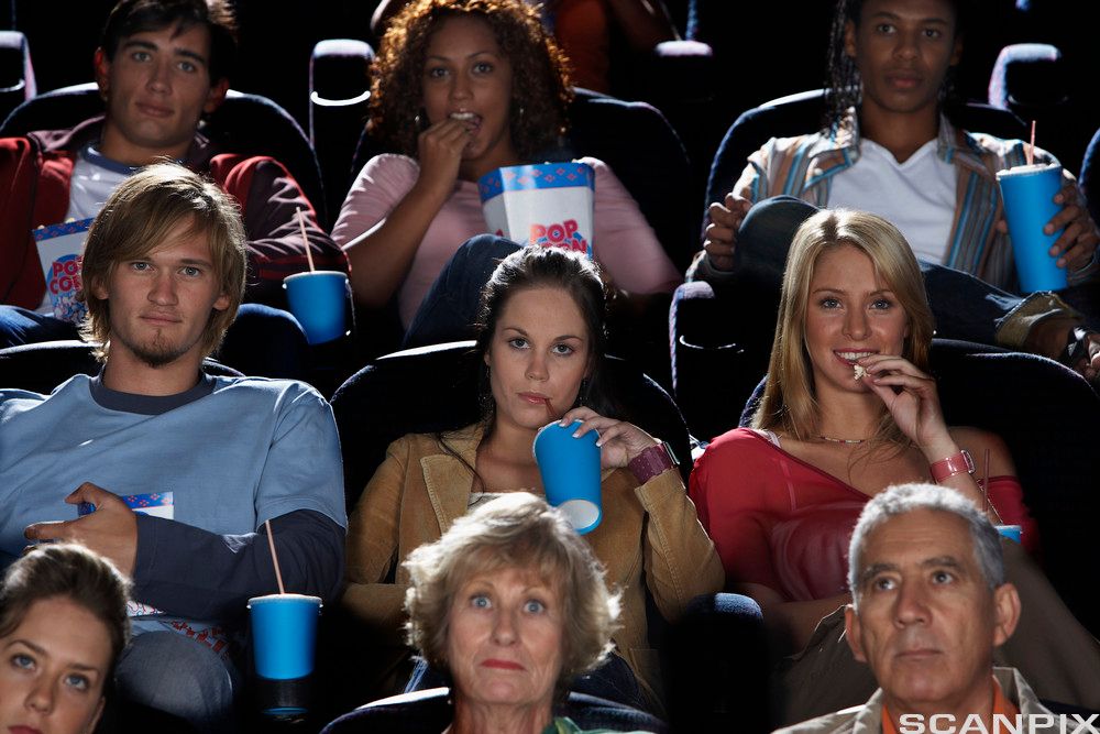 Mange mennesker i en kinosal ser på en film. Noen har pappkurs og esker med popkorn i hendene. De har tilfredse ansiktsuttrykk. Foto.