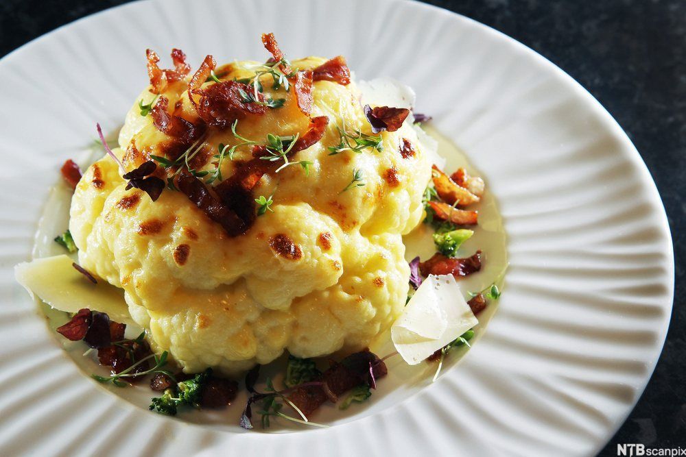 Gratinert blomkål med bacon på en hvit tallerken. Foto.