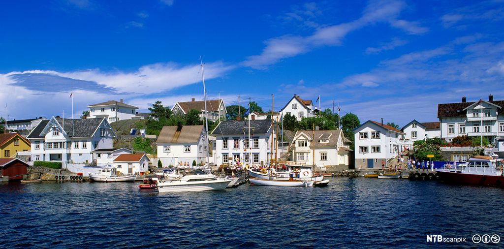 Hvite sørlandshus og båter ved kai. Foto.