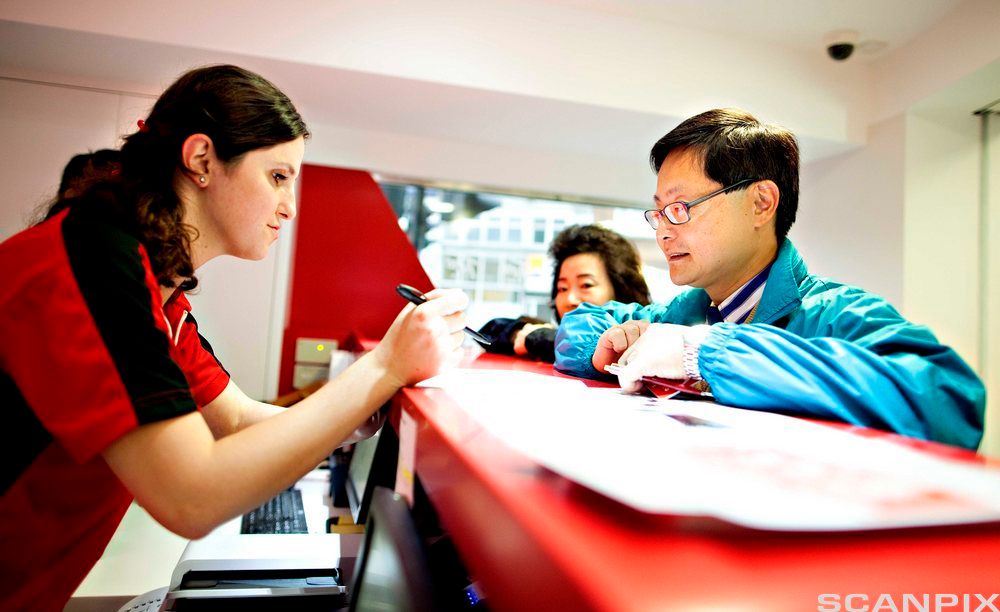 Hotellresepsjonist og gjester. Foto.