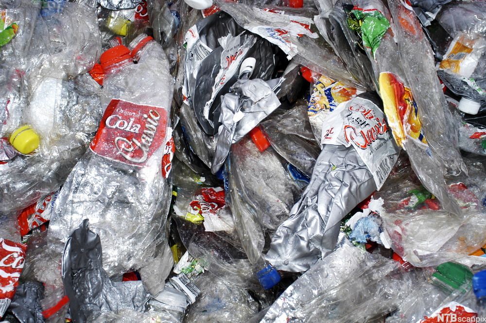 En mengde plastflasker, blant annet colaflasker, er presset flate og samlet i en haug. Foto.