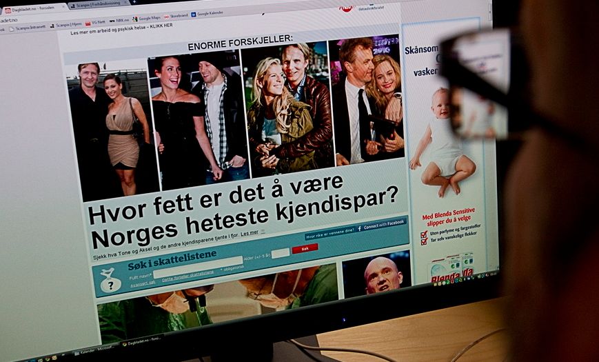 Framsida til ei nettavis fyller ein dataskjerm. Delar av skjermbiletet er reklame. I framgrunnen sit ein person og ser på skjermen. Foto.