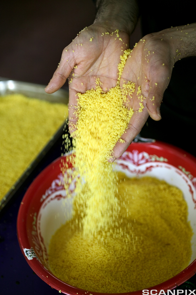 Gule couscous-gryn helles fra ei hånd og ned i en bolle. Foto.