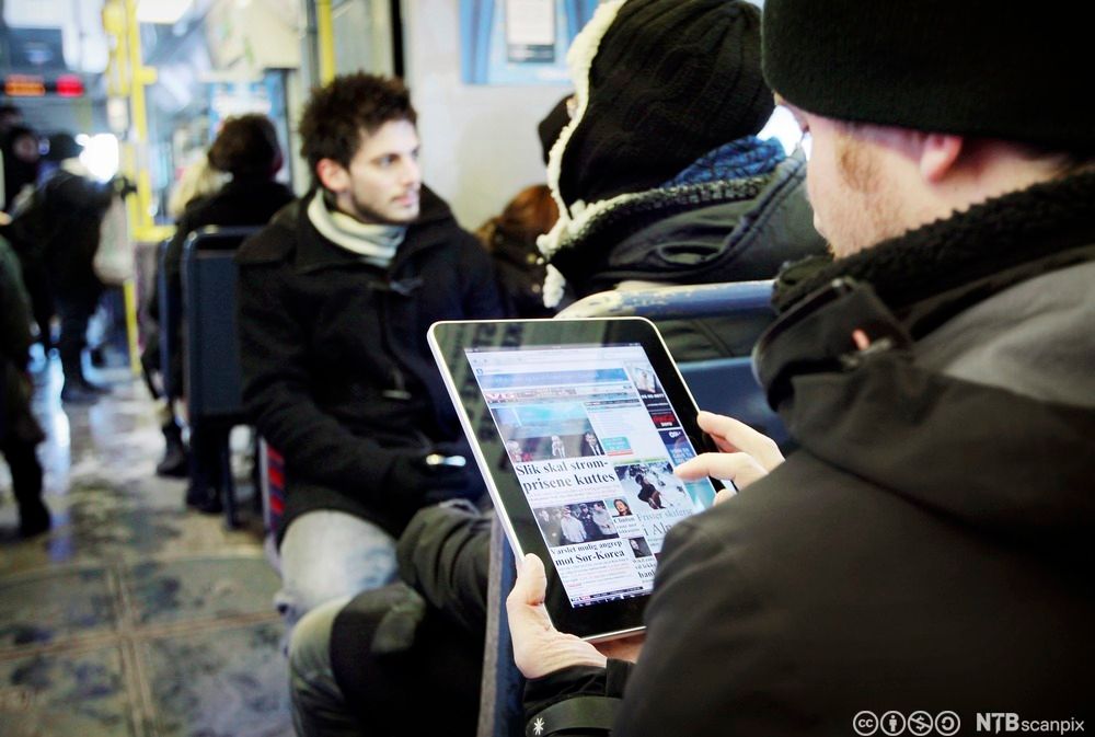 Mann leser avis på iPad på trikken. Foto.