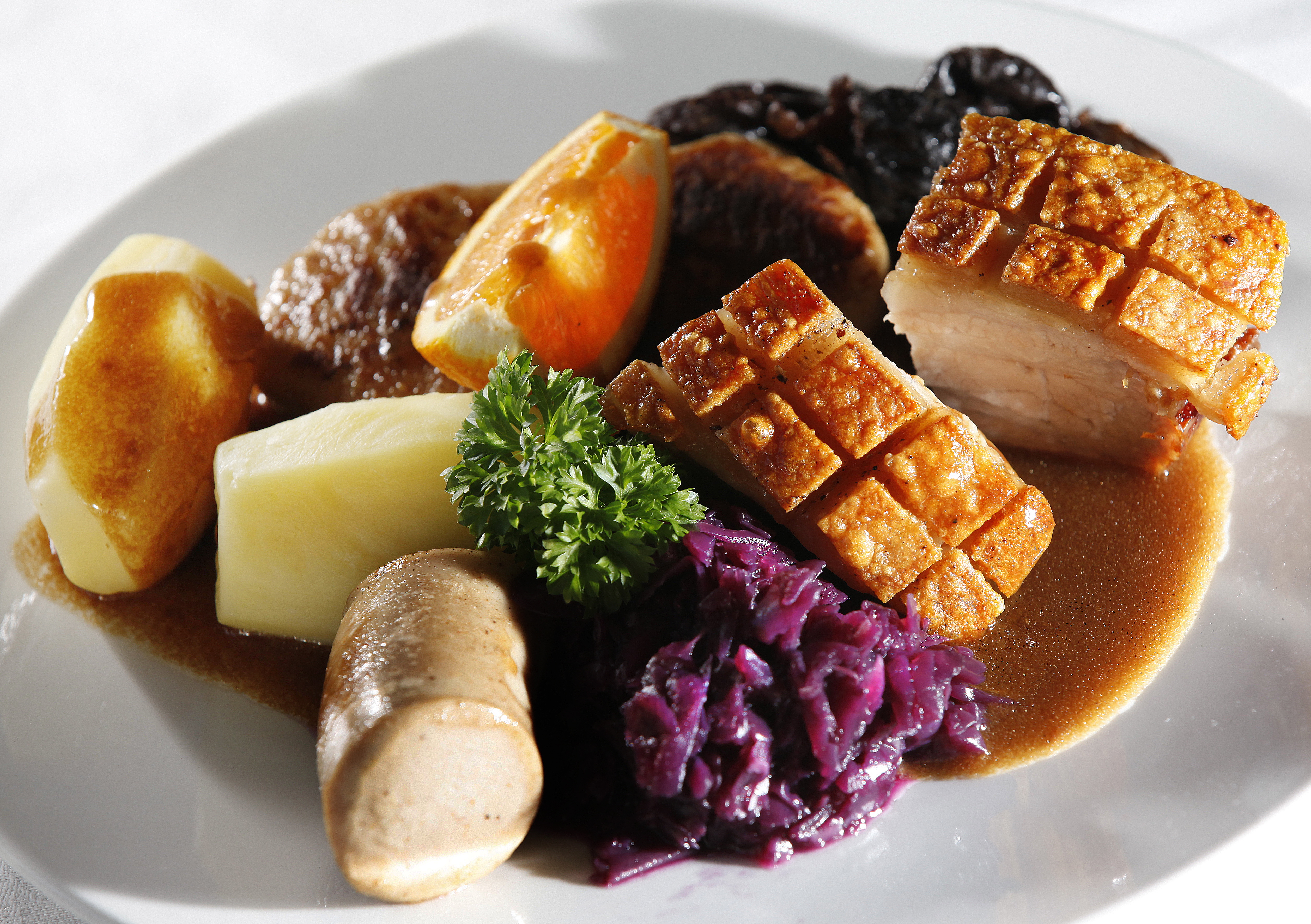 En tallerken med ribbe, potet, rødkål, medisterpølse og brun saus. Foto.