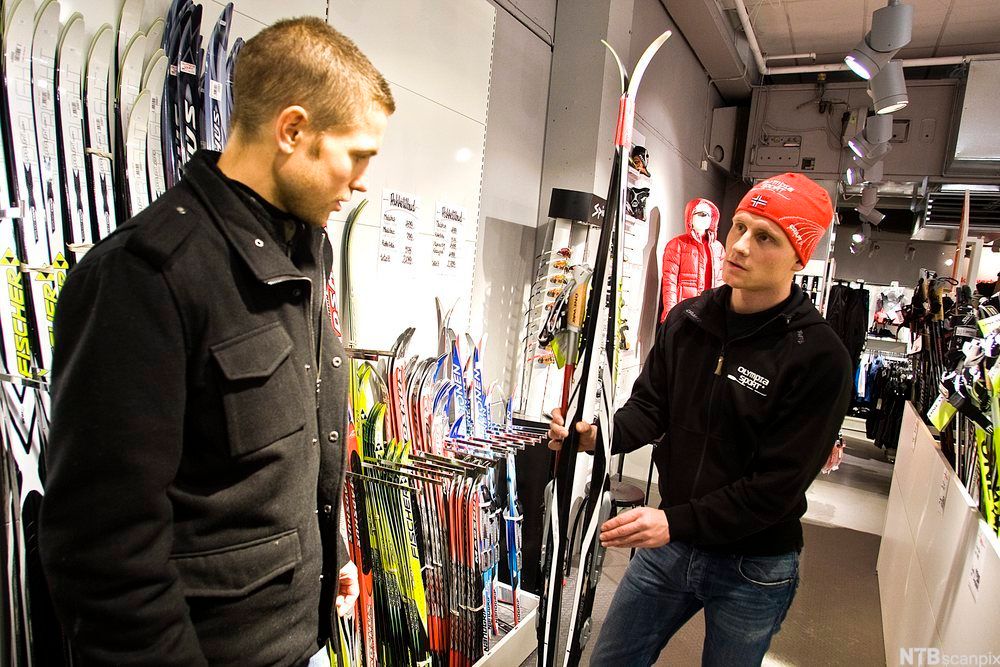 Selger og kunde i sportsbutikk ser på ski. Foto.