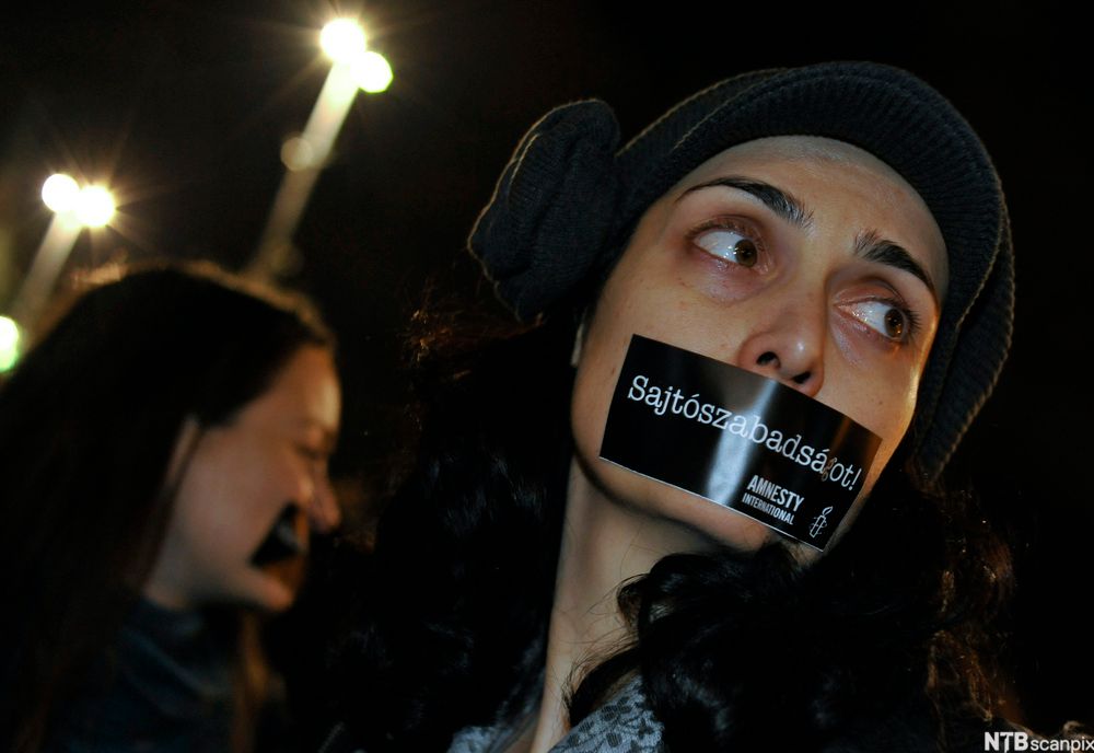 Kvinner deltar i protest mot mediesensur. De har bred, svart teip klistret over munnen. Foto.