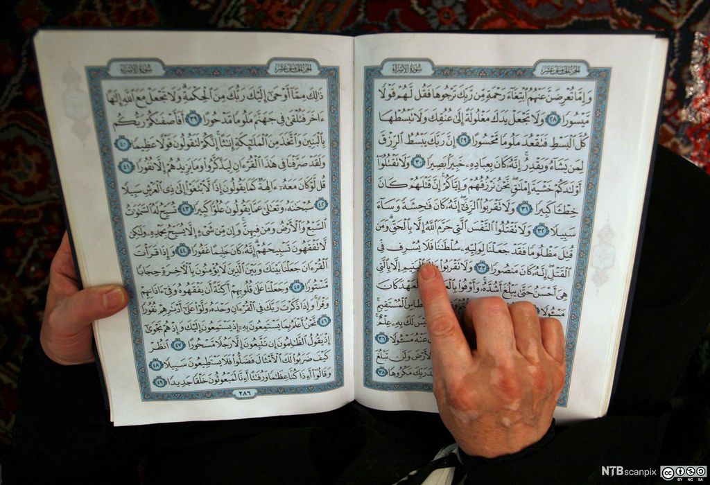 Ei hånd følger linjene i ei bok med arabiske skrifttegn. Foto.