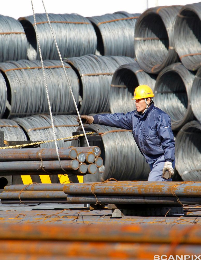 Ein arbeidar flyttar stålstenger og stålkveilar. Foto.
