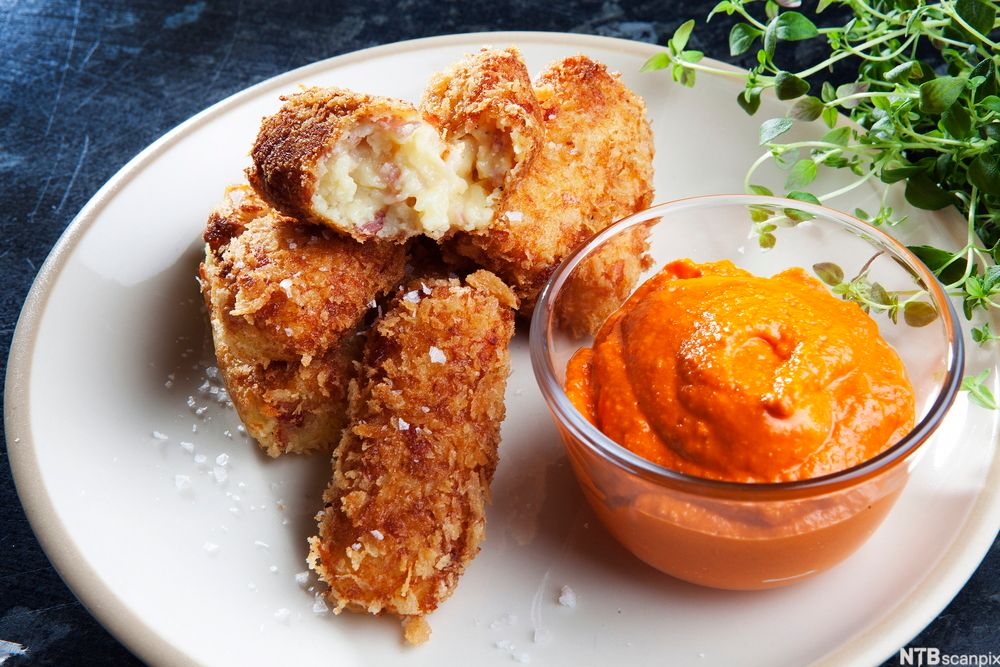 Potetkroketter med ei skål med spansk ost ved siden av. Foto.