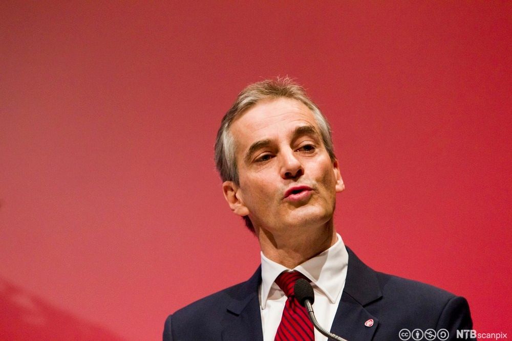 Arbeiderpartiets leder Jonas Gahr Støre på en talerstol. Rød bakgrunn. Foto.