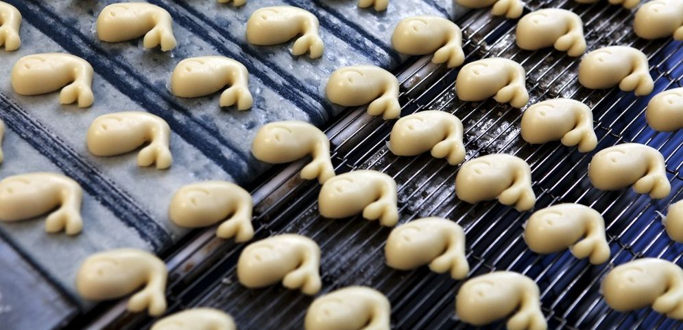 Marsipanbiter formet som små hvaler på et samlebånd. Foto.