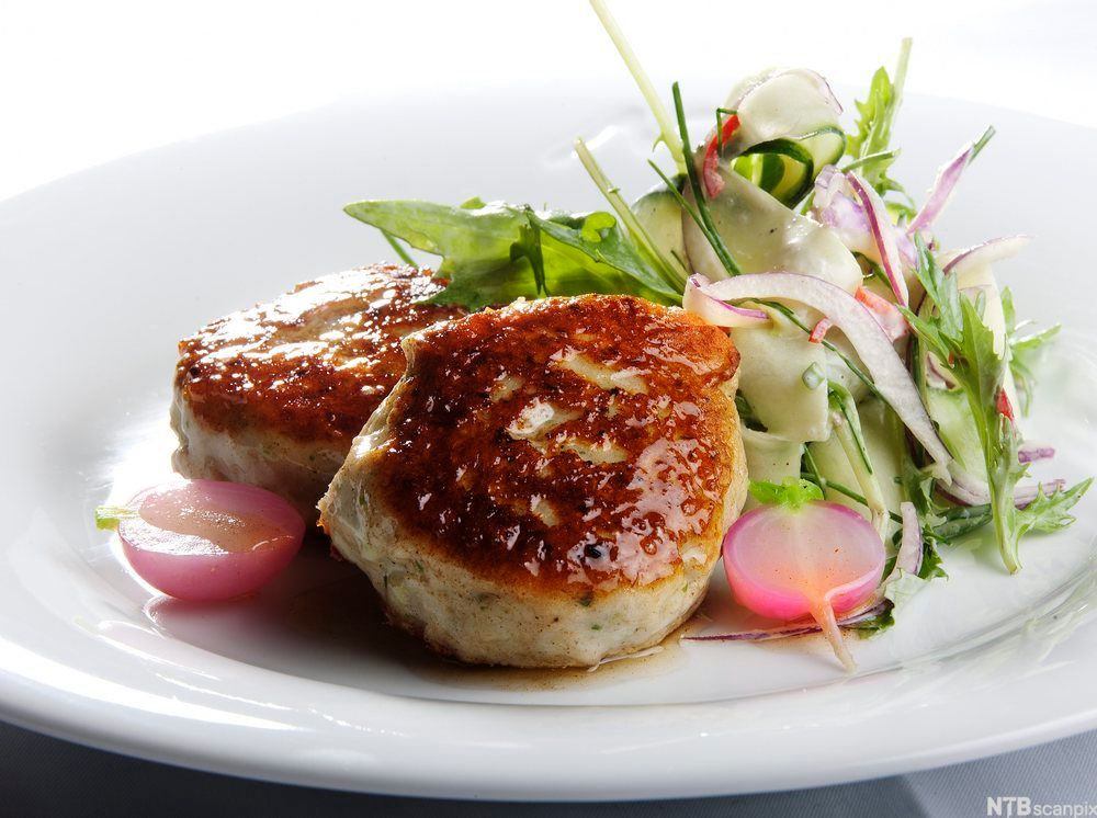 To fiskekaker på en tallerken med en grønn salat. Foto.