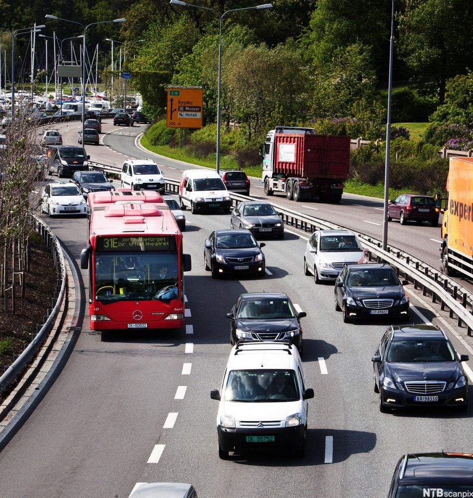 Biler og buss på trefelts motorvei mellom ei bukt med seilbåter og blomstrende syriner. Et skilt peker mot Bygdøy. Foto.