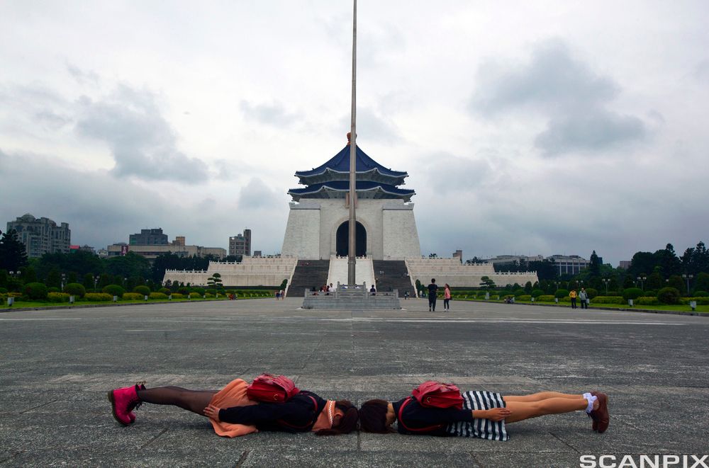 To jenter ligger mot hverandre på bakken med ansiktet ned. Foto. 