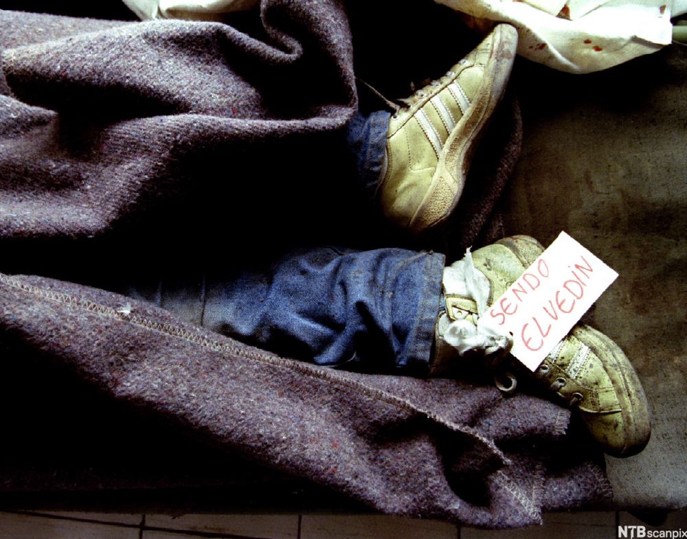 Bilde av føttene til en liten gutt som har dødd under et bombeangrep. Resten av kroppen er dekka av et teppe.