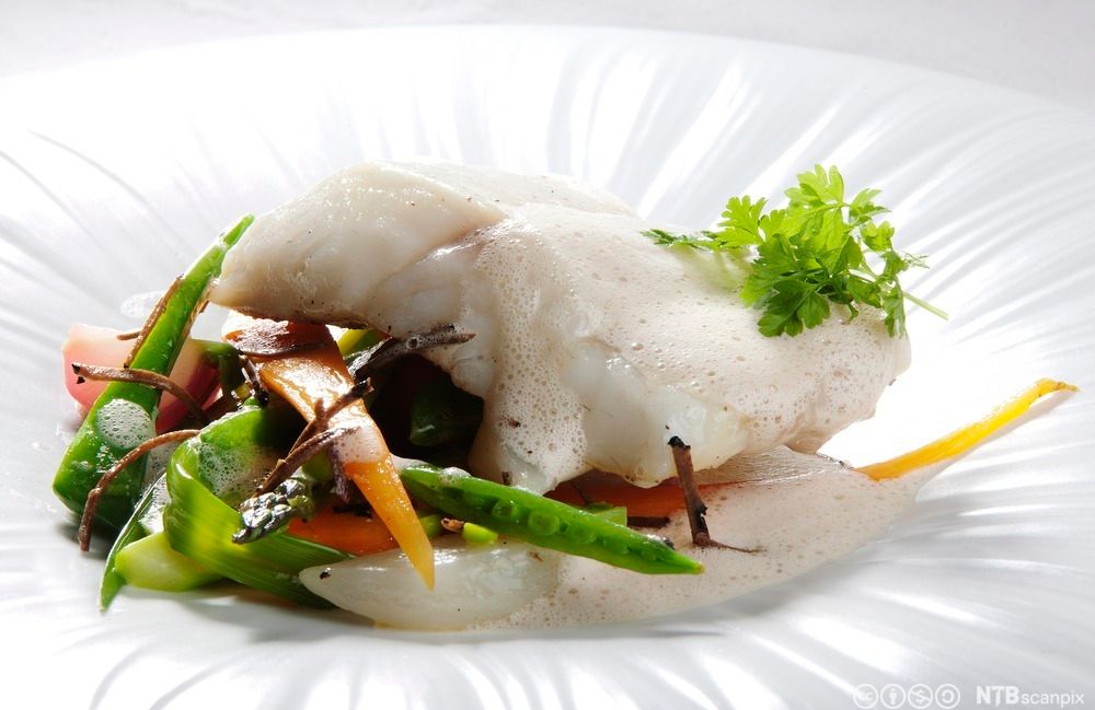 Hvit fisk med skummende, lys saus, stekte grønnsaker og persille. Foto.