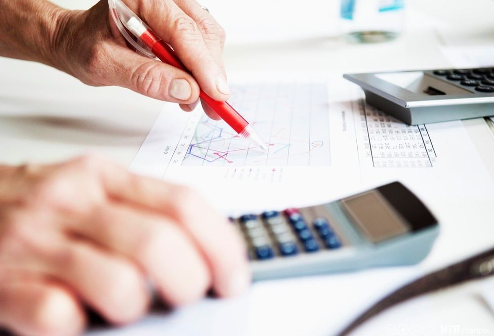 Hender, kulepenn, kalkulator og et ark med en graf og en tabell. Foto.