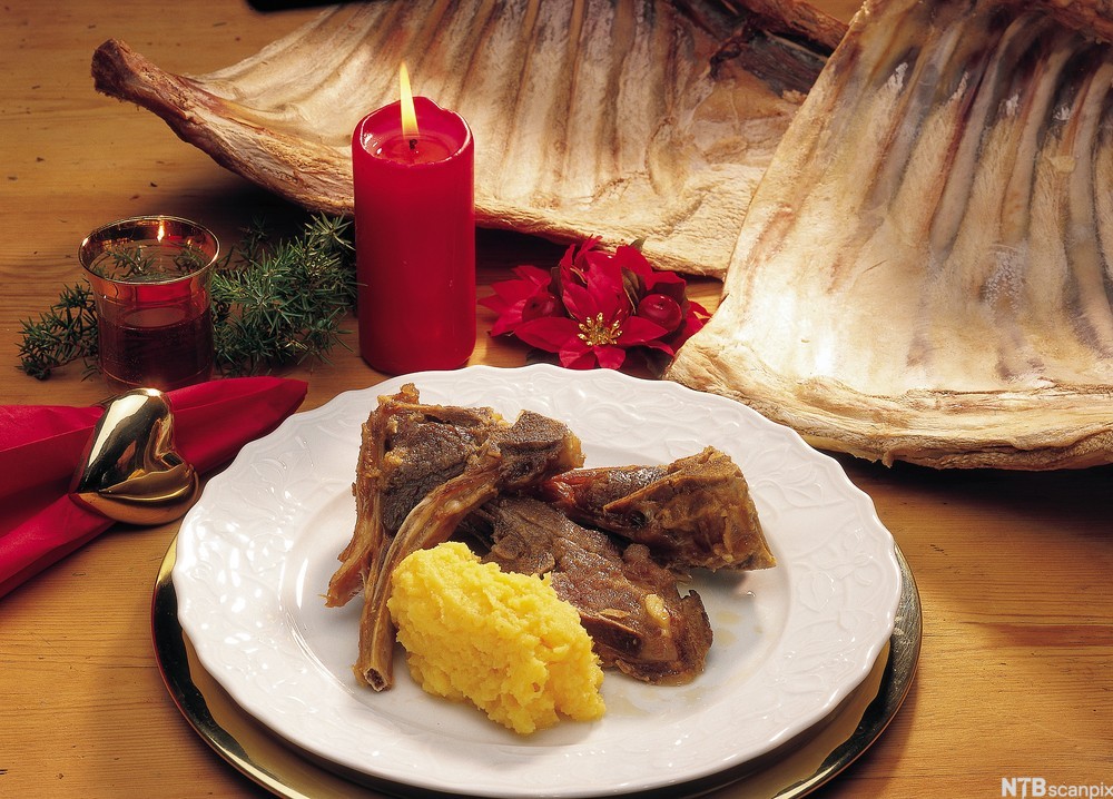 Pinnekjøttallerken med kålrotstappe anrettet på hvit tallerken. Det står et rødt kubbelys og andre juledekorasjoner på bordet. Foto.