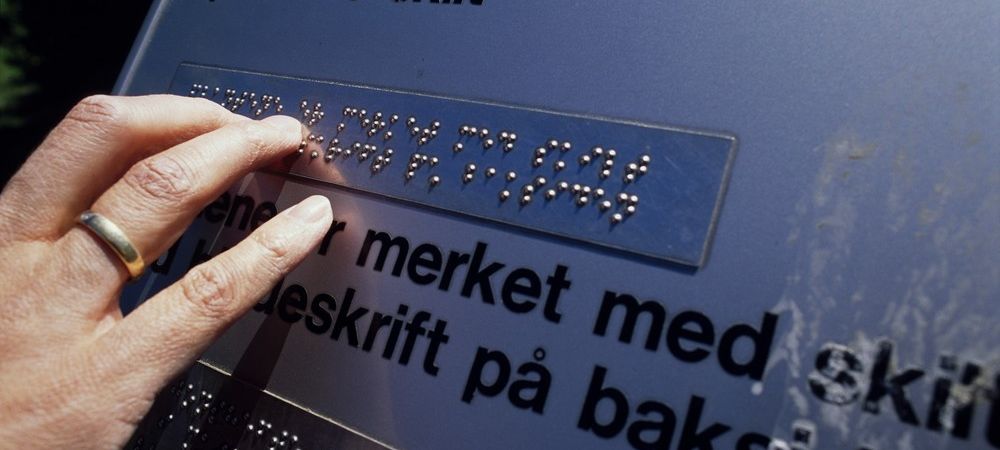 Hand les punktskrift på ei informasjonstavle. Foto.
