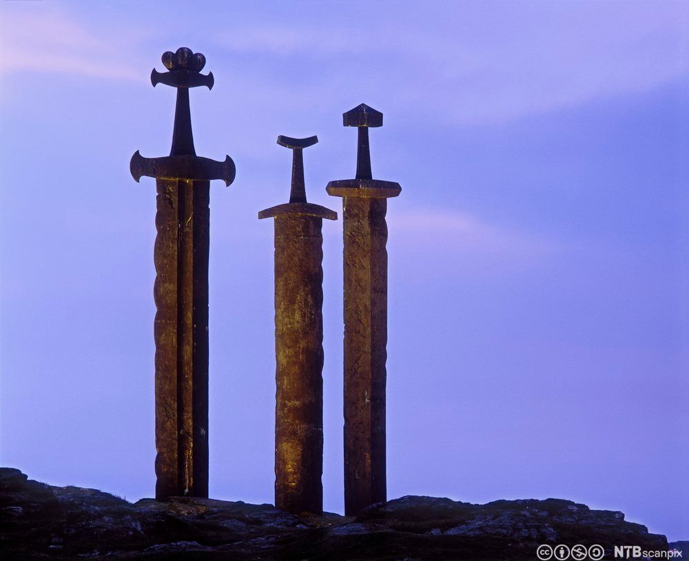 Tre store sverd i metall som er stukket ned i fjellet. Foto.