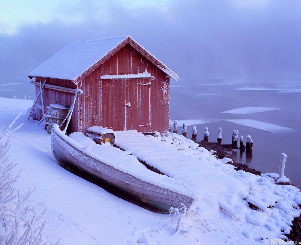 Båtnaust i vinterlandskap med en snødekket båt ved siden av. Foto.