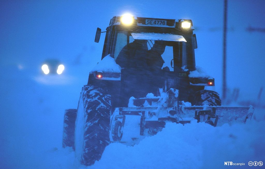 Traktor brøyter vei i mørket i snøstorm på Karmøy. Foto.