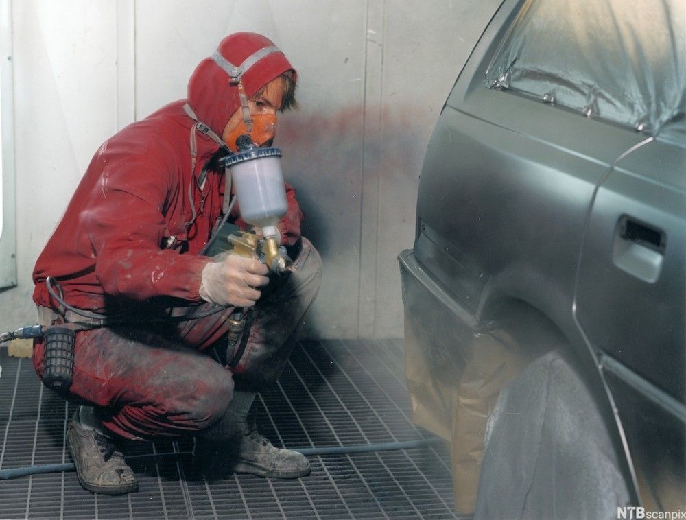 En mann med lakksprøyte sitter på huk ved siden av en bil.