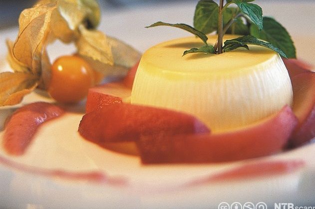 Råmjølkspudding på ei skål, pynta med eit grønt blad og physalis. Foto.